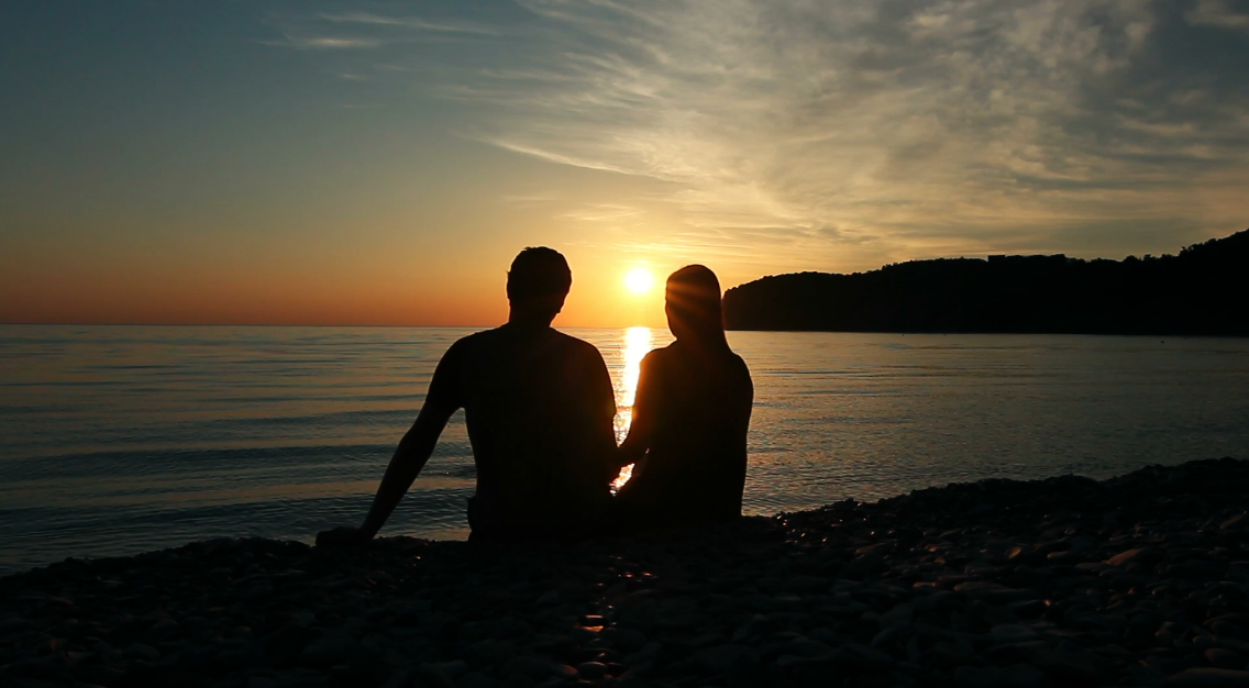 浪漫的情侣日落时坐在海边的沙滩上约会视频素材